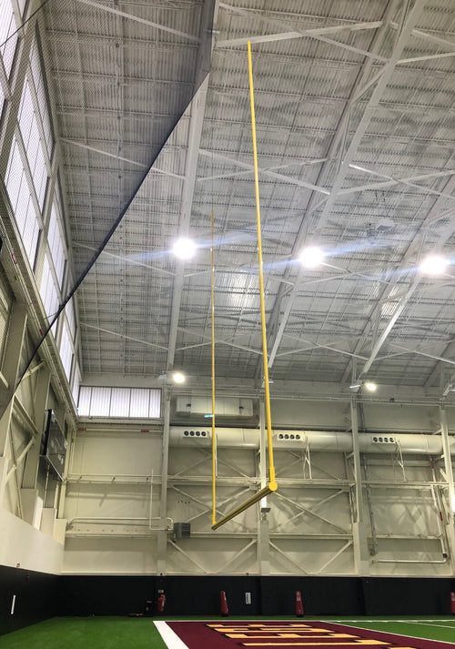 Yellow football goalposts hanging from a high ceiling in an indoor sports facility.
