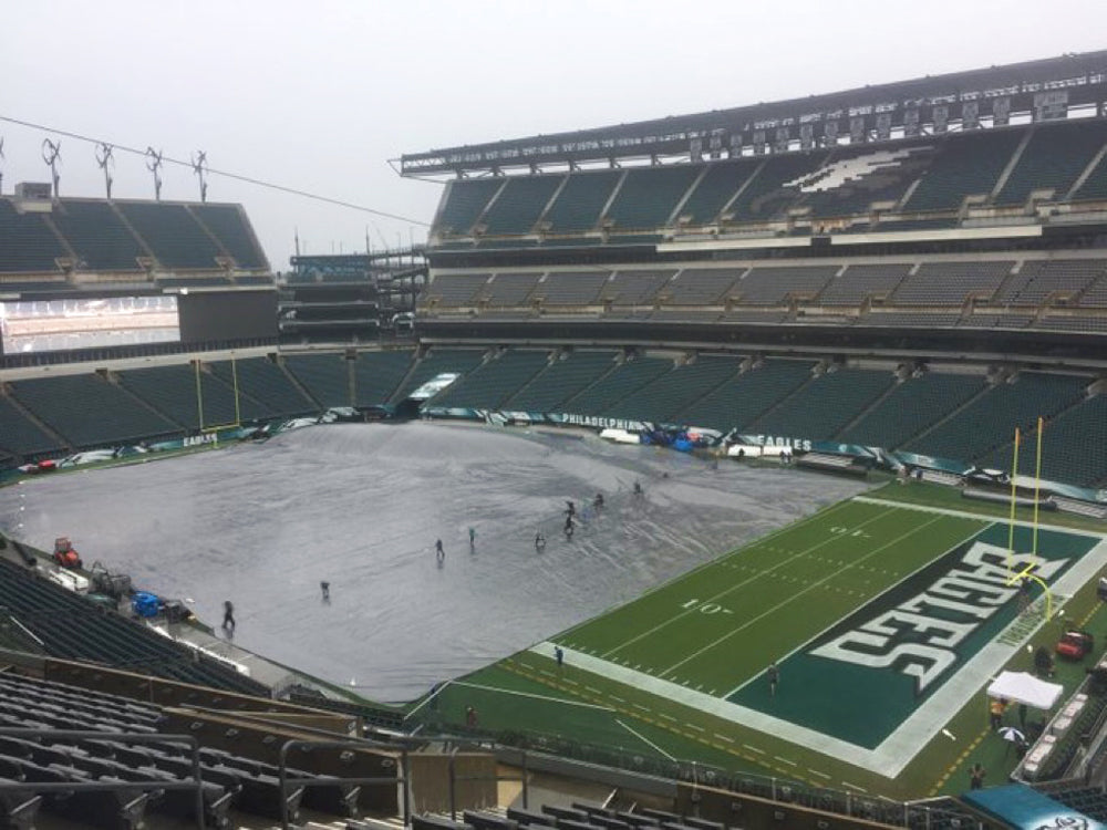 Grounds crew pulling a large football field cover across the turf at Lincoln Financial Field, with the green Eagles end zone still exposed