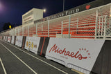 Football windscreens printed with Michael's Bakery and other sponsor logos along a stadium track at Heartland Field