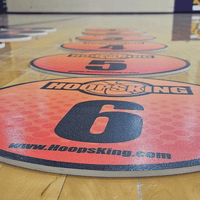 Thumbnail for Orange and black numbered spot markers on a wooden basketball court floor.