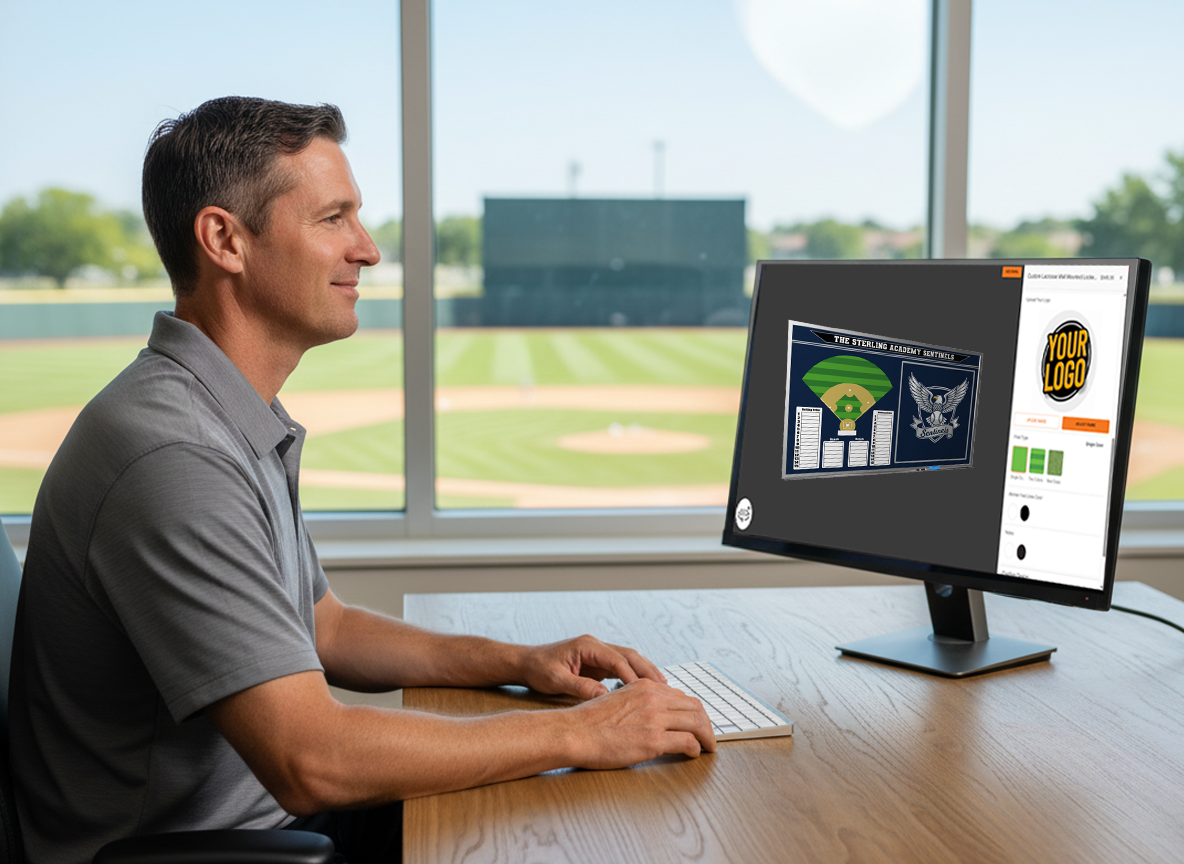 Athletic director viewing a digital proof of a Sterling Academy Sentinels custom baseball whiteboard on a monitor in a sunny office overlooking a baseball field.