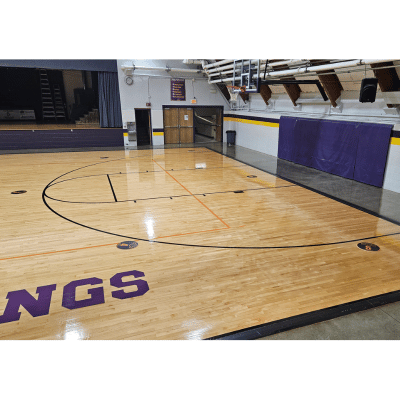 Basketball court with four black spot markers on the floor, purple wall padding, and a stage.