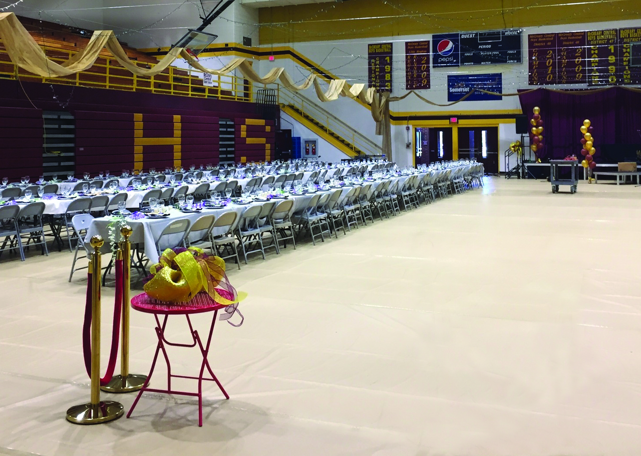 Tan gym floor covering protecting basketball court during school banquet with draped tables and formal place settings