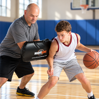 Thumbnail for Coach using the black HoopsKing Toughness Training Pad beside a young basketball player practicing ball protection in a school gym.