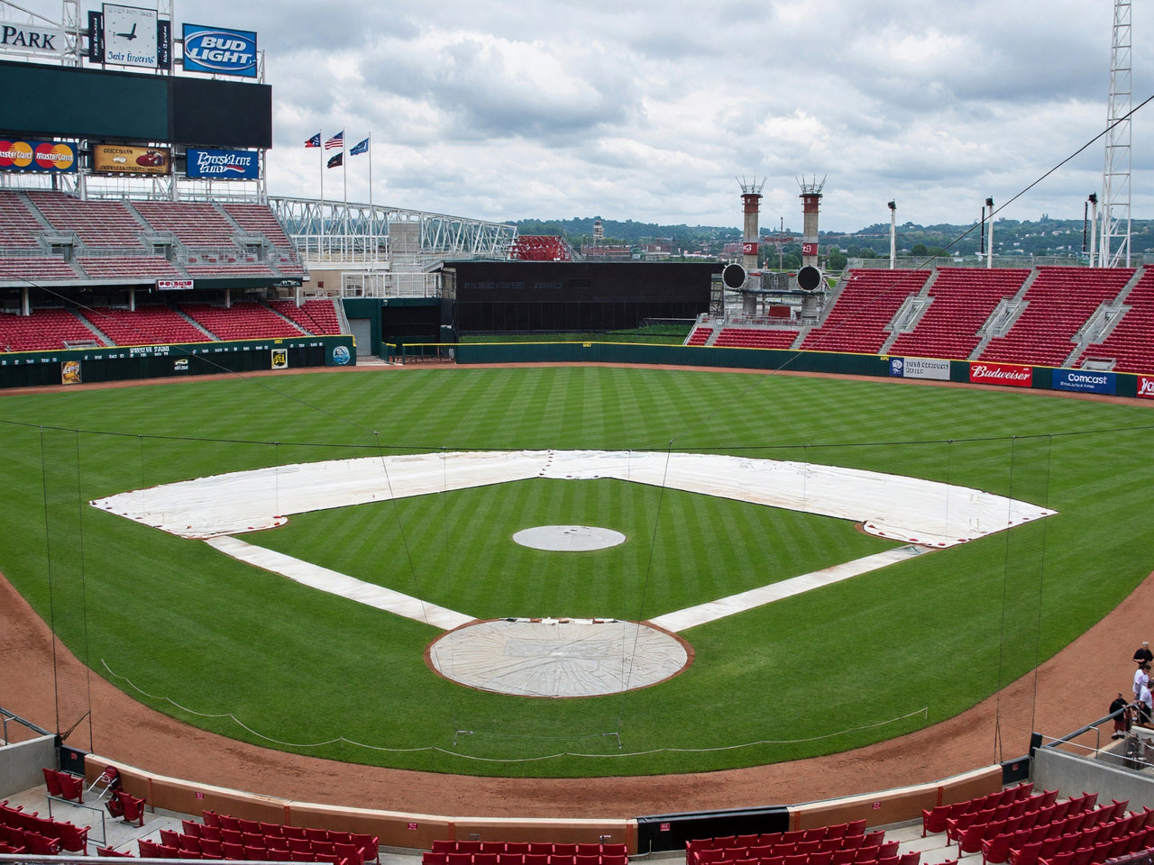 White skin tarps covering the base paths and infield dirt of a baseball diamond, with round covers on the pitcher's mound and home plate in an empty ballpark