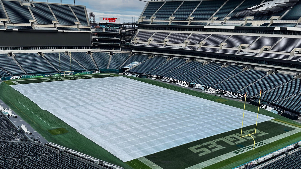 Lincoln Financial Field stadium interior showing a CoverSports growth cover deployed across the Philadelphia Eagles NFL field between the end zones, with the Eagles logo visible on the seatback covers and the team name displayed on the sideline barrier