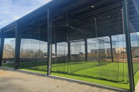 Thumbnail for Covered outdoor batting cage system with multiple hitting cages, steel frame construction, netting, and artificial turf at an athletic training facility