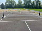 Pickleball net on an outdoor court with white lines, black posts, and a paved surface.