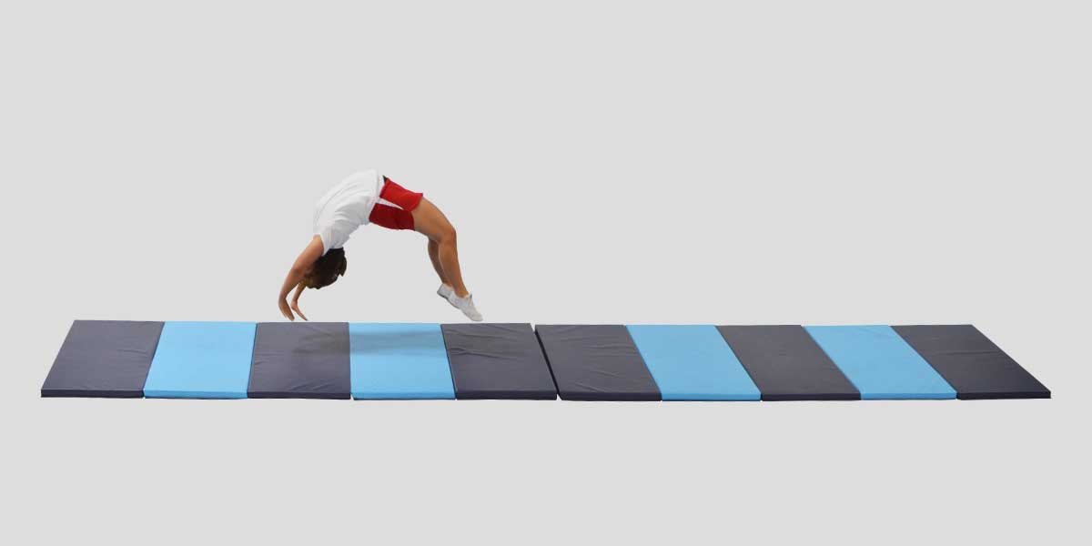 Gymnast doing a backbend on a long, folding blue and gray polyethylene mat.