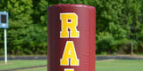 Large maroon goal post pad with gold sewn lettering on a stadium upright