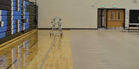 Thumbnail for Gym floor partially covered with beige protective mats, revealing hardwood floor and bleachers.