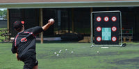 Thumbnail for Baseball player pitching towards a black target with red and white bullseyes on a green turf field.