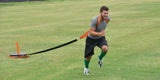 Man running on grass, pulling a weighted sled with a harness and strap.