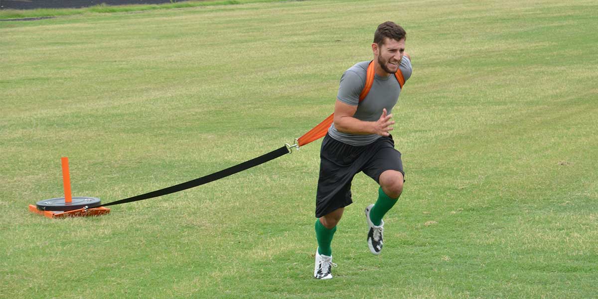 Man running on grass, pulling a weighted sled with a harness and strap.