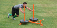 Thumbnail for Man pushing an orange push-pull sled with weights across a grassy field.