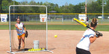 Softball pitcher behind a protective net, throwing to a batter.