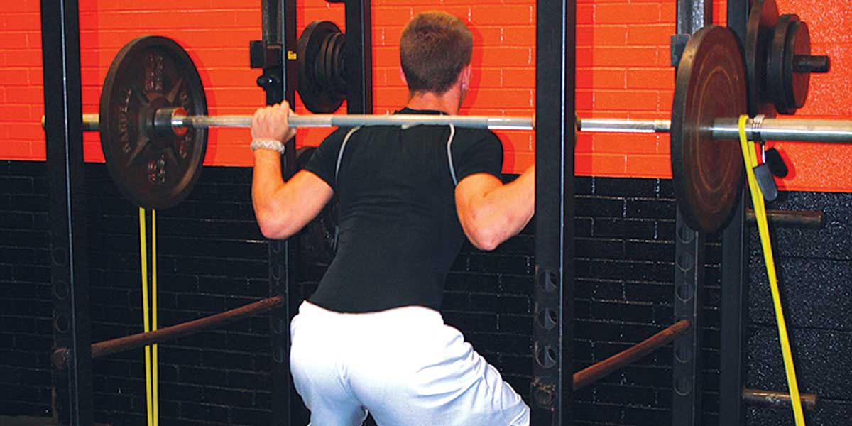 Man squatting with a barbell, resistance bands attached to the barbell and squat rack.