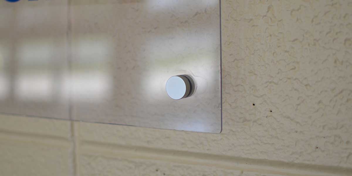 Clear acrylic wall sign mounted with a silver standoff on a textured beige wall.