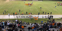 Thumbnail for High angle view of a high school football game at night, with fans in the stands and players on the field.
