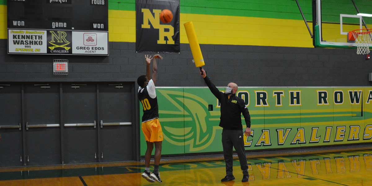 Basketball player shooting a ball while a coach holds a yellow foam stick.