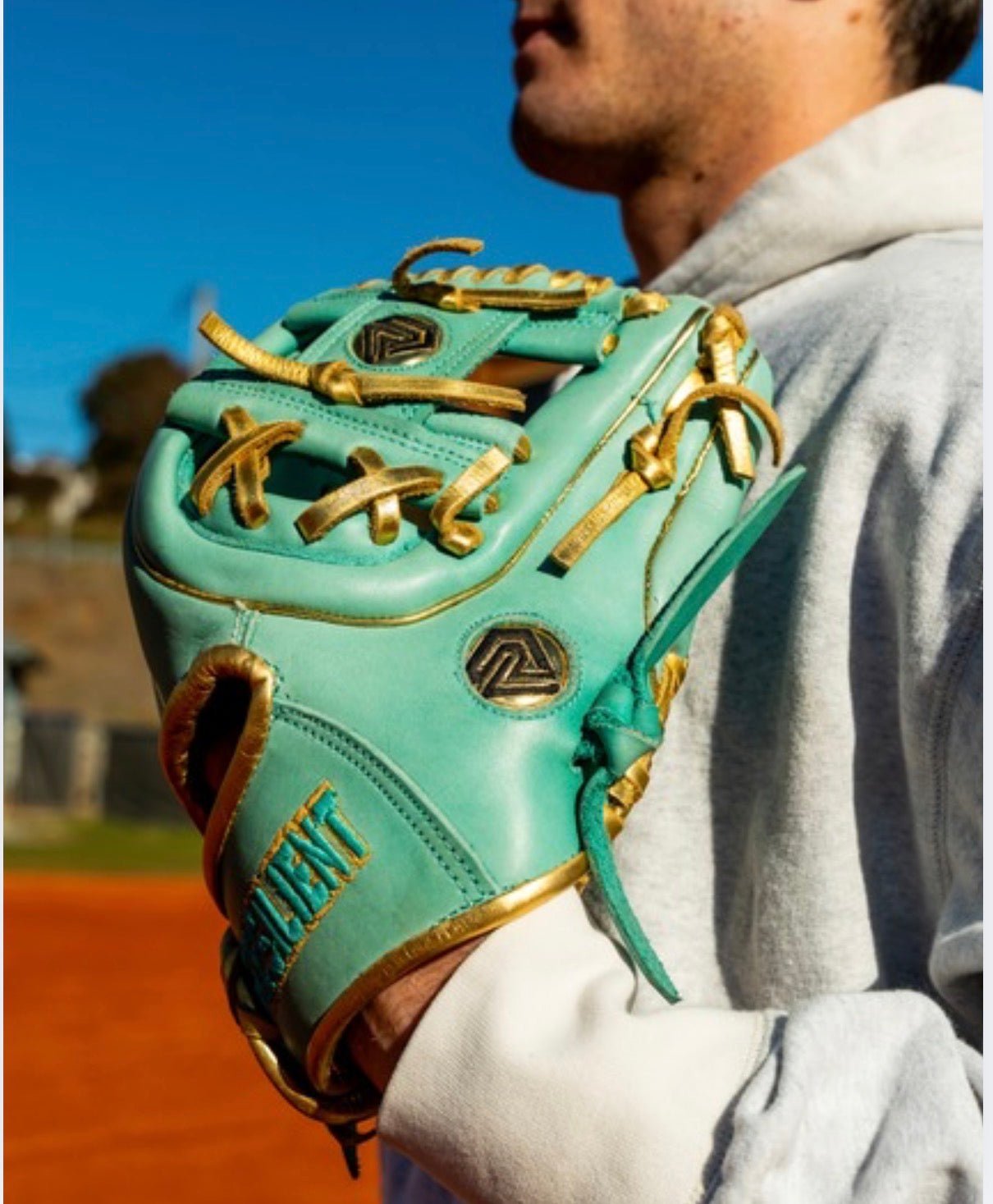 Mint green baseball glove with gold laces and trim, held by a person in a gray hoodie.