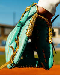Thumbnail for Mint green baseball glove with gold lacing, held by a person, on a sunny baseball field.