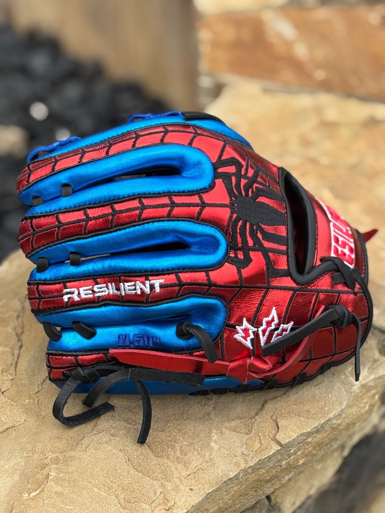 Red and blue baseball glove with black spider web design, "RESILIENT" text, and white maple leaf logo.