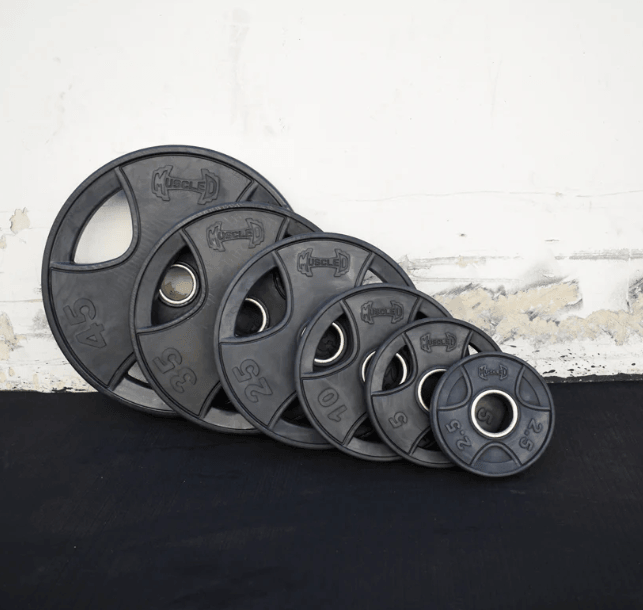 Set of black rubber Olympic weight plates in various sizes, leaning against a white wall.