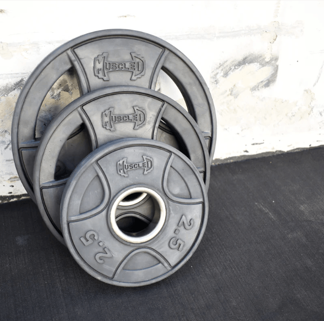 Three black rubber Olympic weight plates of varying sizes, with "MUSCLE" and "2.5" visible on the front.