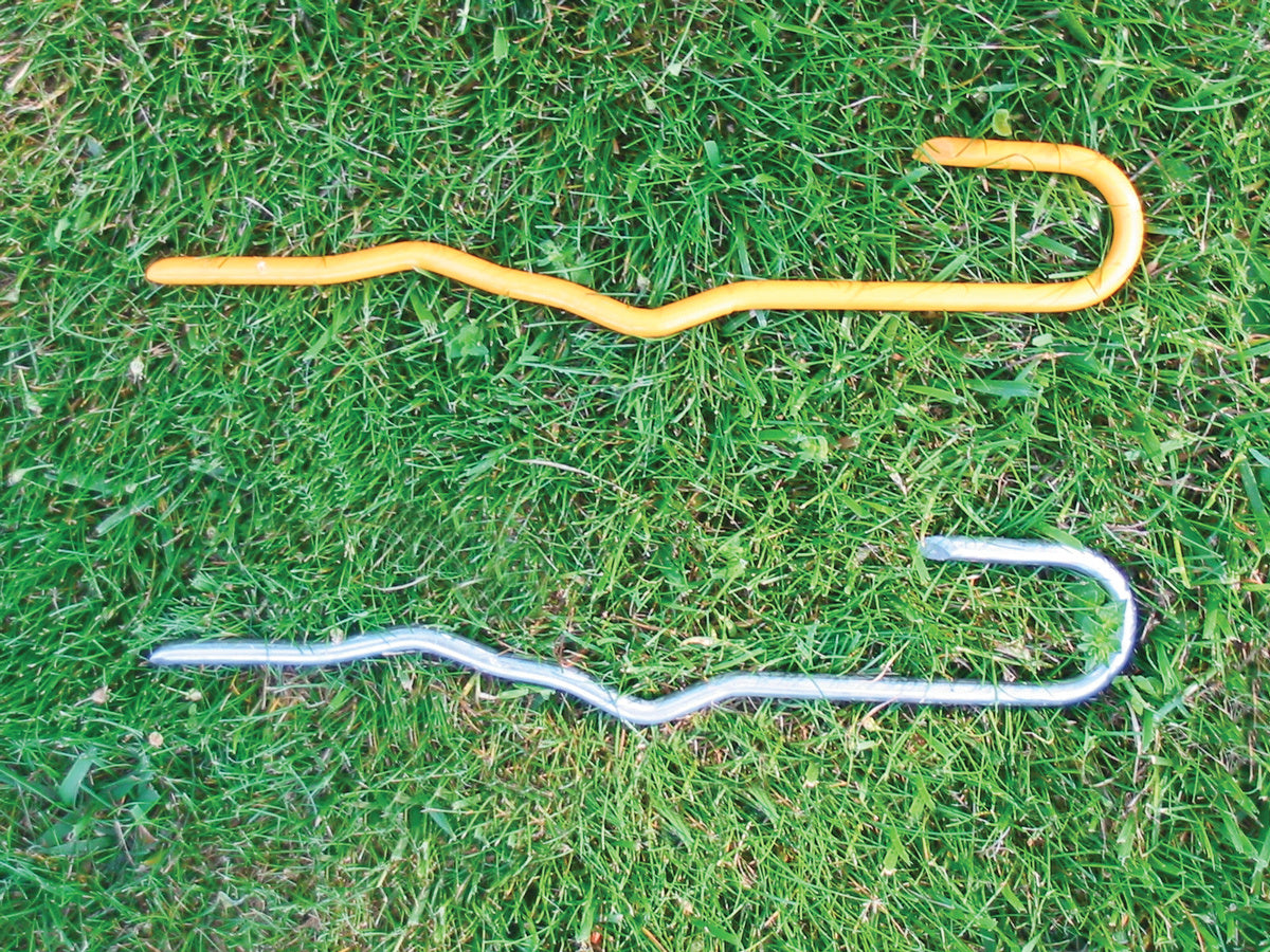 Yellow and silver metal hook stakes for tennis court covers lying on grass