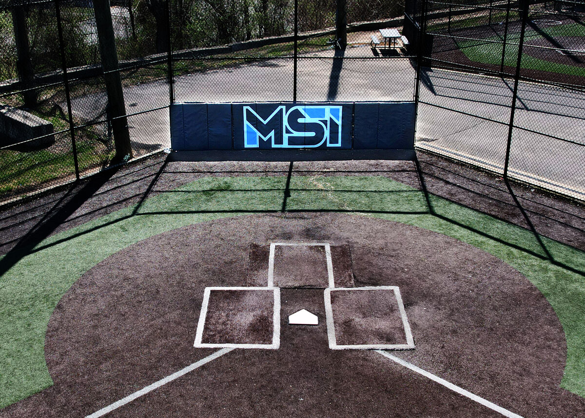 Navy backstop padding with a light blue MSI logo behind home plate in an outdoor batting cage