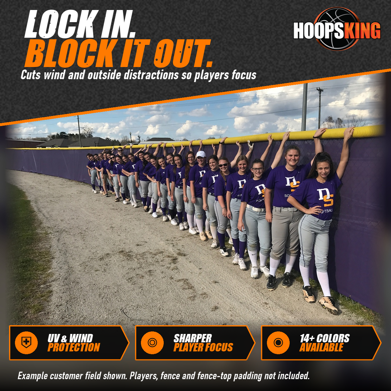 Softball team in purple shirts lined up against a purple outfield fence windscreen below a yellow fence top