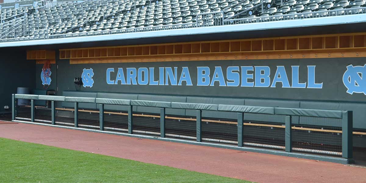 Green square rail padding along a dugout below a Carolina Baseball wall