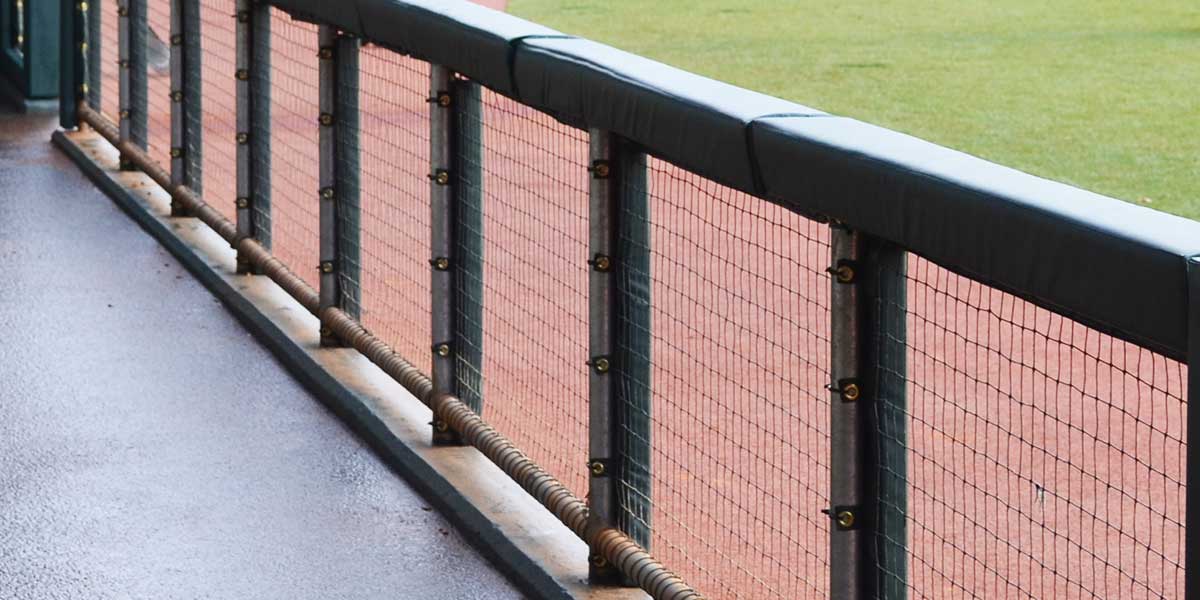 Green square padding on the top rail of a dugout fence with netting below