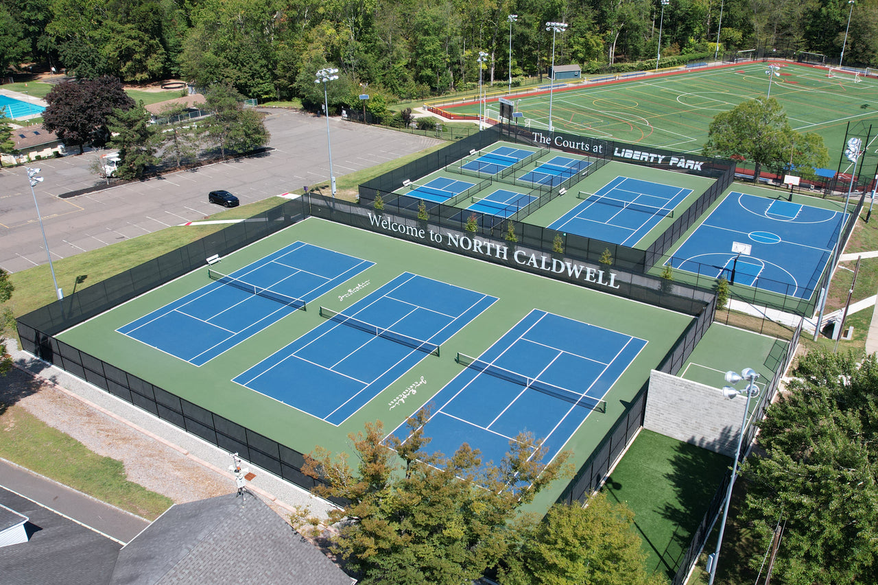 Aerial view of tennis courts surrounded by custom printed privacy screens featuring facility branding at The Courts at Liberty Park in North Caldwell