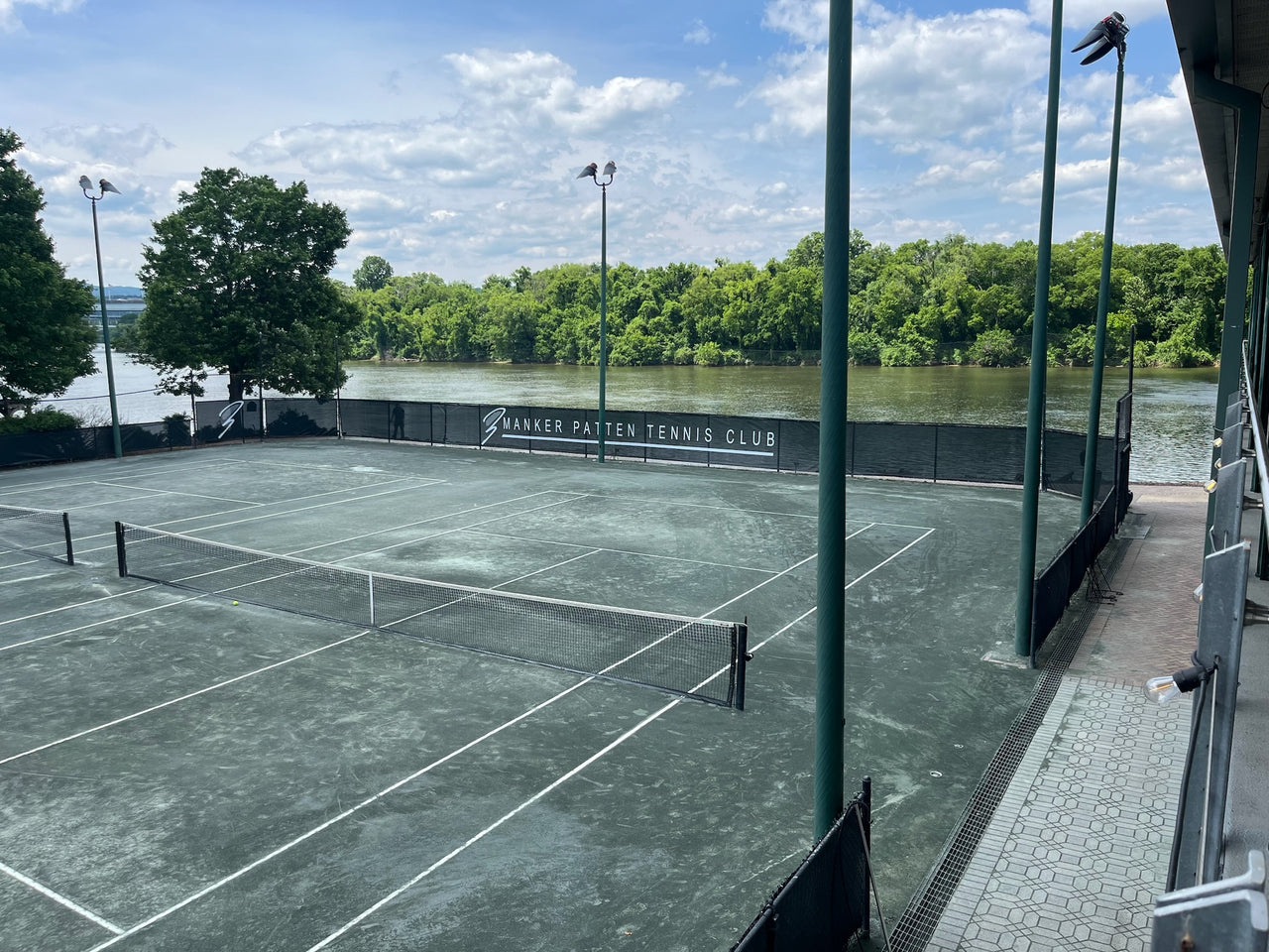Black classic mesh tennis court windscreen with custom printed club logo installed along chain link fence at Manker Patten Tennis Club