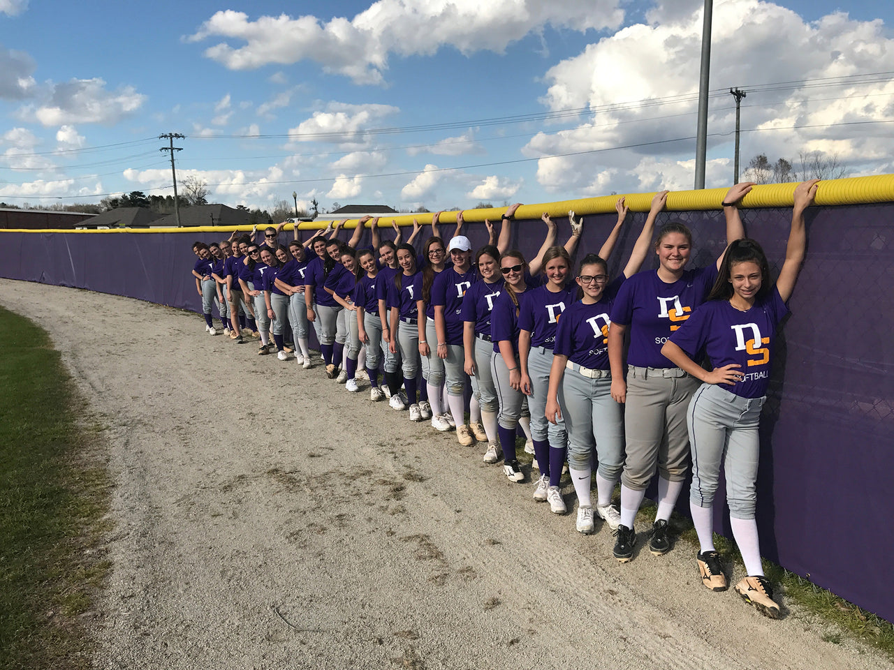 High school girls' softball team lined up against the outfield fence windscreen
