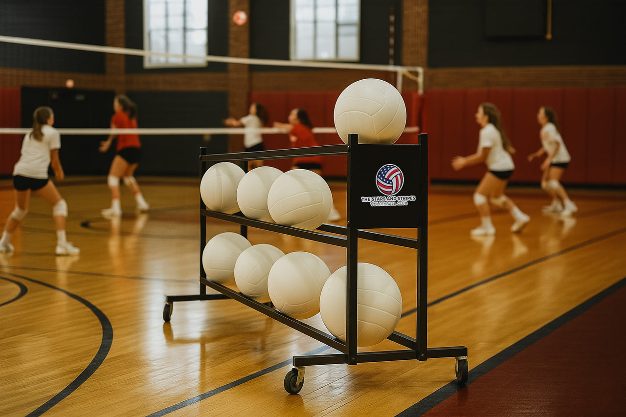 Black rolling ball rack with 7 white volleyballs on a gym court with players in the background.