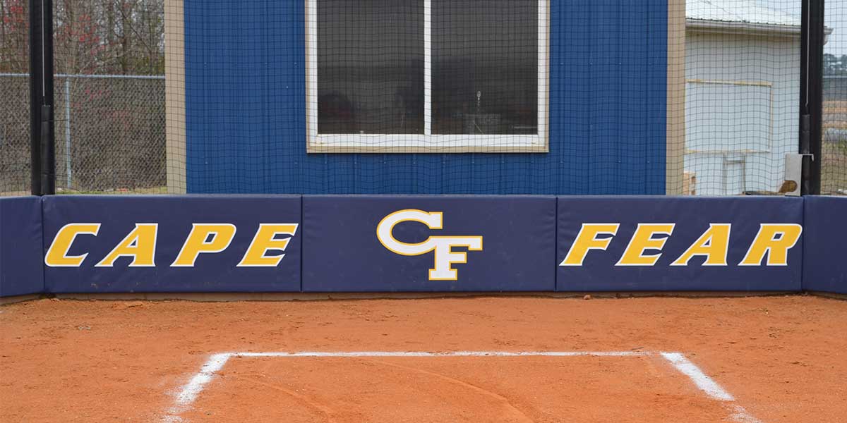 Navy L-shaped backstop wall padding printed with Cape Fear behind home plate