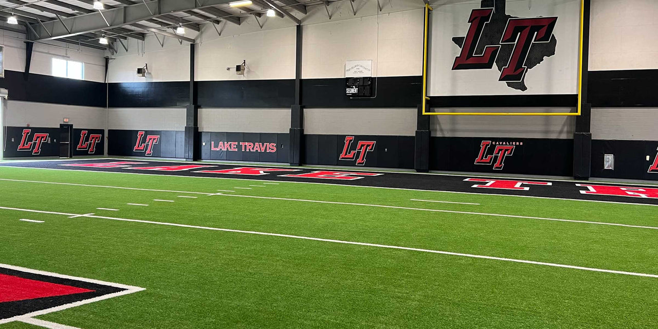 Black wall padding with printed team logos lining an indoor turf training facility