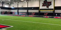 Thumbnail for Black wall padding with printed team logos lining an indoor turf training facility