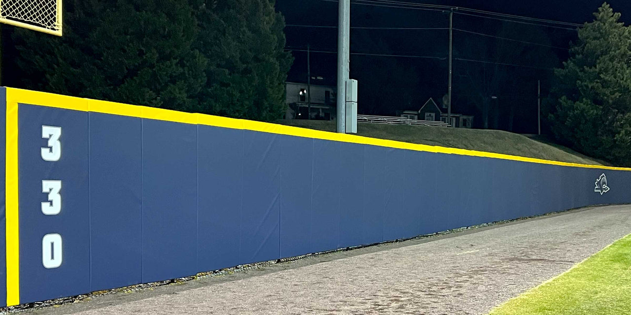 Navy outfield wall padding with a yellow top edge and a 330 distance marker at a college baseball field