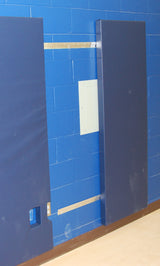Blue wall pads attached to a blue brick wall with Z-clips, revealing a white electrical panel.