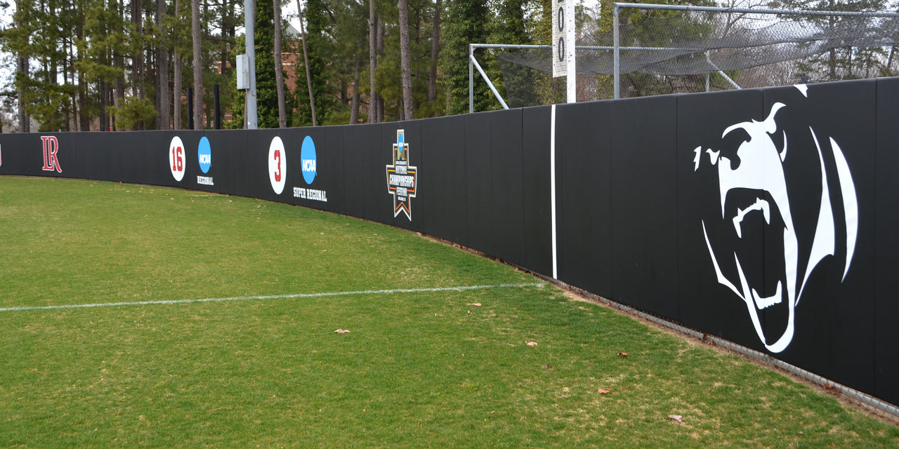 Black softball outfield wall padding with a printed bear logo and retired numbers